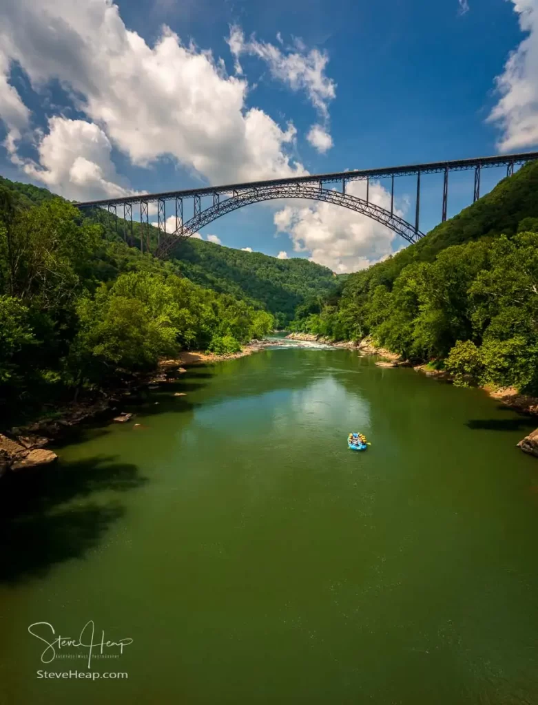 Vertical view of the New River flowing under the famous bridge with rafters paddling towards the rapids. Prints in my online store