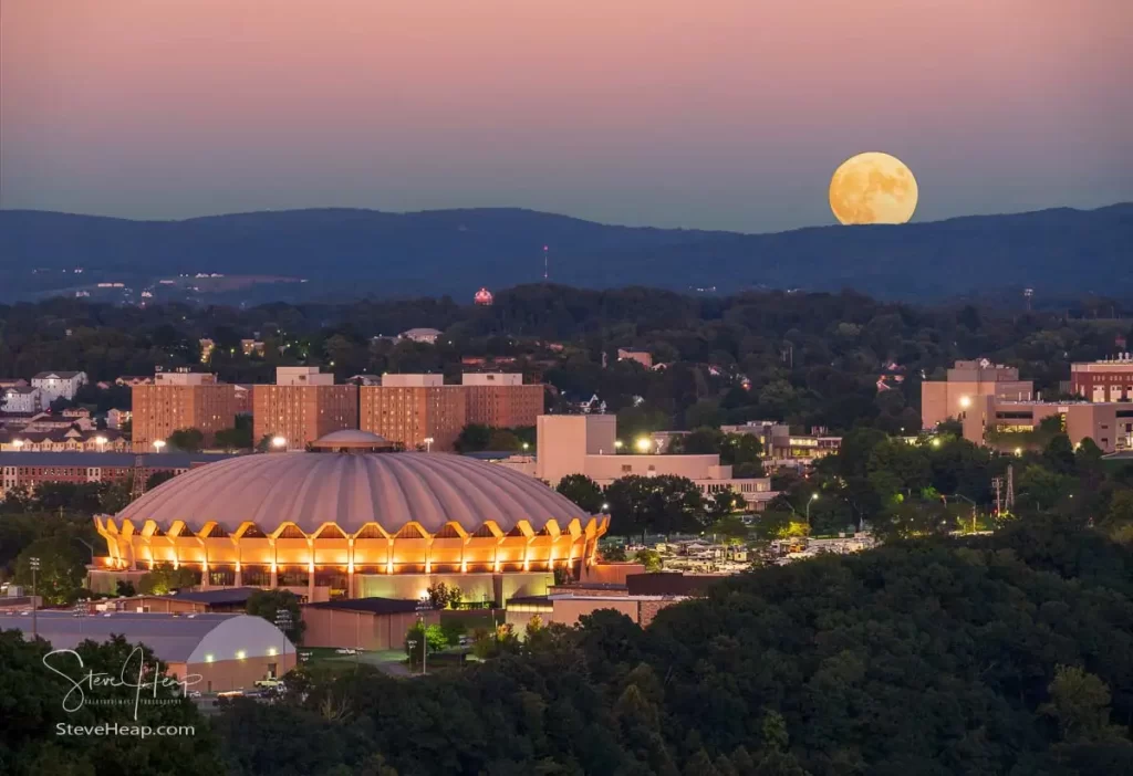 Moon rising over the hills surrounding Morgantown with the illuminated Coliseum in the foreground on the Evansdale Campus of WVU