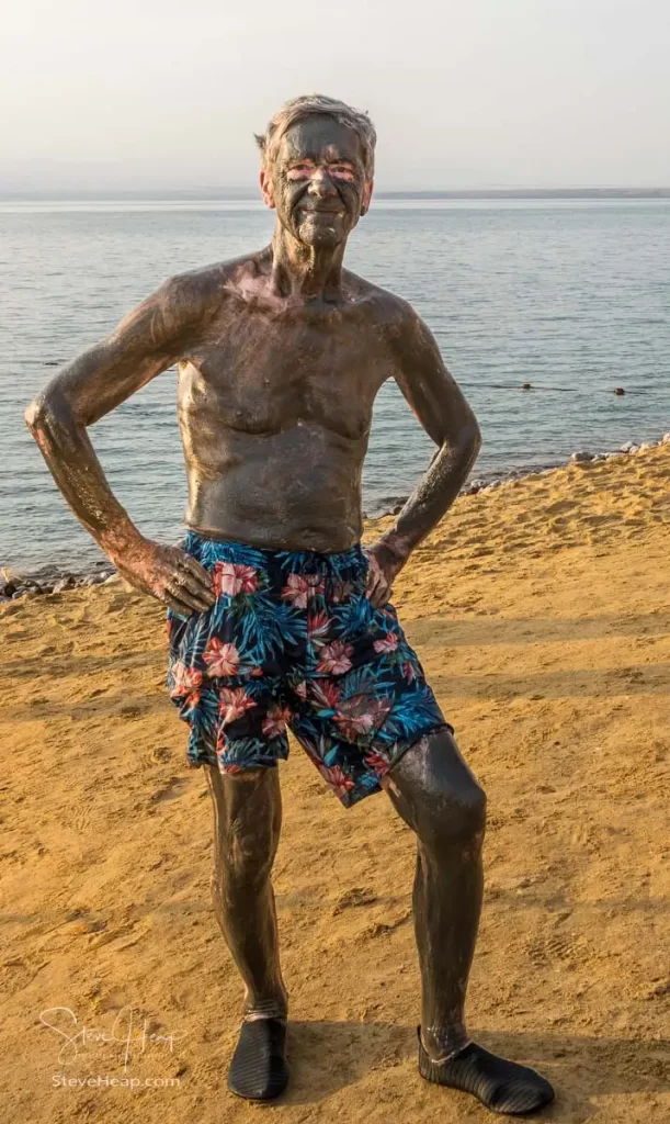 Man covered from head to foot in the salty black mud from the bottom of the Dead Sea