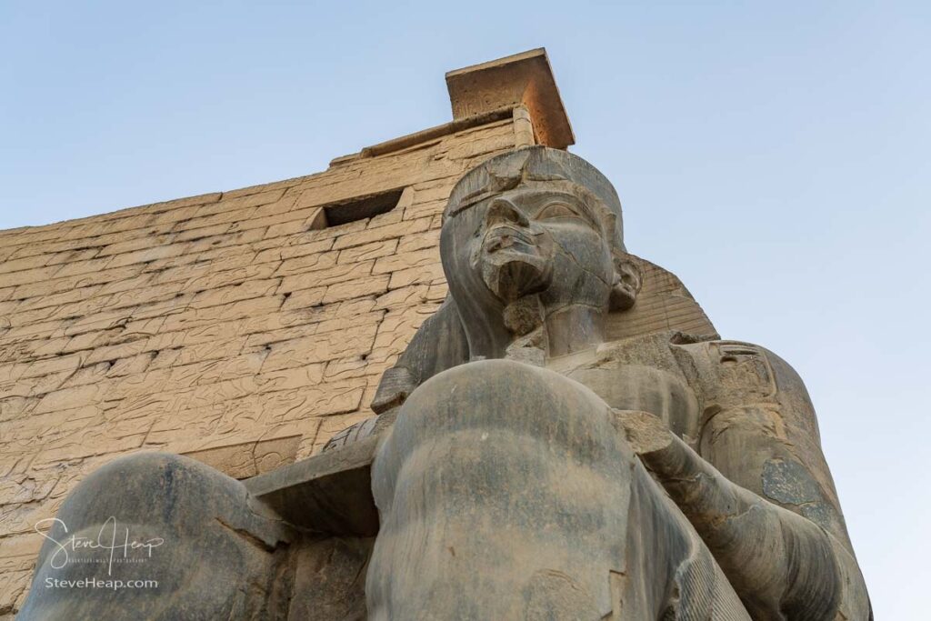 A massive stone statue of Ramesses II stands in Luxor temple, showcasing intricate carvings under the warm glow of the setting sun.