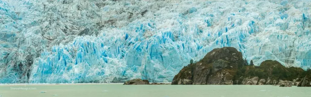 Trees growing on the rocks with the massive glacier ice piled up behind as it slowly makes its way into the ocean. Prints available in my online store